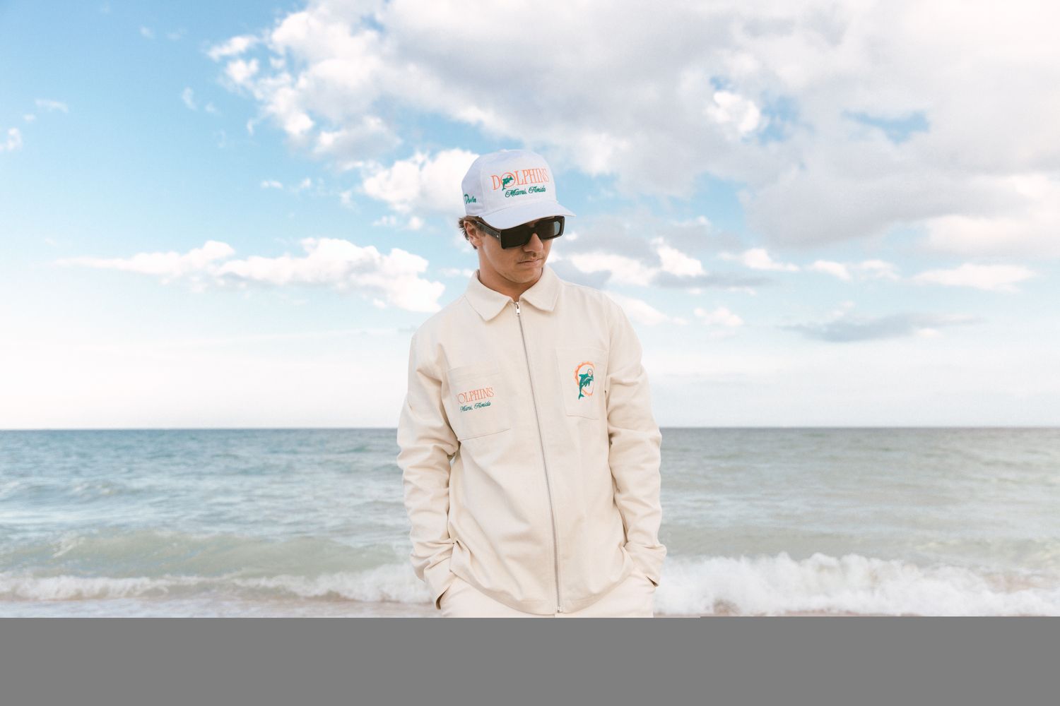 A man models Miami Dolphins apparel on a beach.